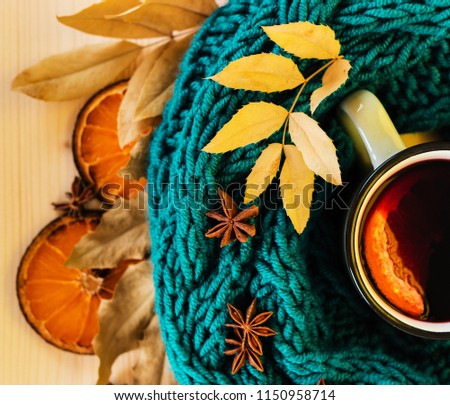 Autumn, fall leaves, hot steaming cup of glint wine and a warm blue scarf on wooden table background. Seasonal, autumnal hot wine, Autumn relaxing and still life concept. Top view.
