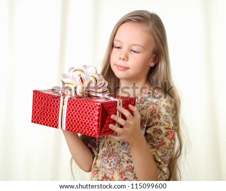 Little blond girl holding a red glamorous gift and looking on it