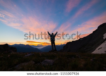 Man standing on mountain top outstretching arms, sunrise light colorful sky scenis landscape, conquering success leader concept. Royalty-Free Stock Photo #1151007926
