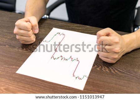 Businessman sitting at table. There are sheet of paper with a trading chart on the table. Angry gesture with hands. Concept photo.
