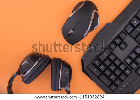 Black mouse, the keyboard, the headphones are isolated on a orange background, the top view. Flat lay gamer background.Workplace with a keyboard, mouse and headphones on a orange background.Copyspace