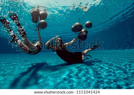 Underwater shoot of flying two women with black balloons