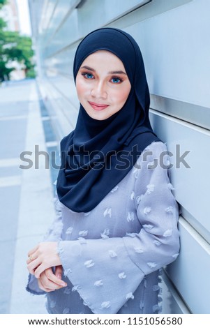 Portrait of a young Muslim woman in a hijab leaning on a railing in the park. She is wearing a blue turban and is elegantly dressed she is of Arab  Malay  Asian descent and is attractive.