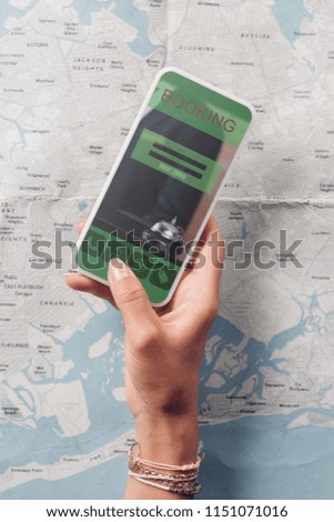 partial view of woman holding smartphone with booking website on screen and map on background