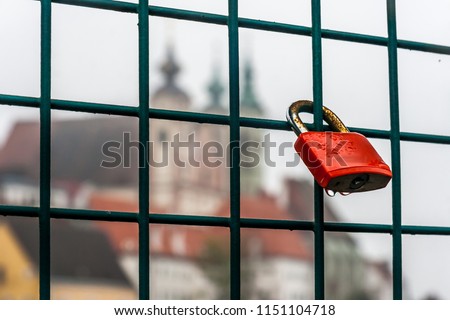Symbolic love padlock fixed to the railings of a bridge in Steyr, Austria. Shallow depth of field and creamy bokeh, with the Saint Michael's Catholic Church in background. Royalty-Free Stock Photo #1151104718