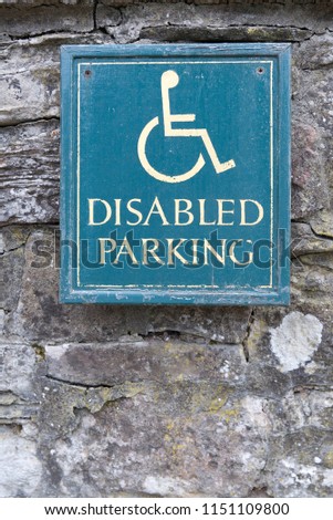 Disabled Parking sign with yellow text and man person in wheelchair symbol with green background on an old stone wall