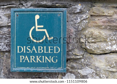 Disabled Parking sign with yellow text and man person in wheelchair symbol with green background on an old stone wall