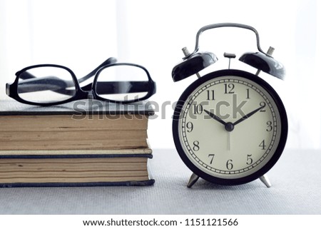 alarm clock, spectacle and books over white curtain. selective focus