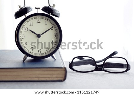 alarm clock, spectacle and books over white curtain. selective focus