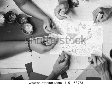 Markers in male and female hands draw on white paper. Hands hold colorful markers and draw kids illustration, top view. Artists wooden table with paints and colored paper. Art and artwork concept.