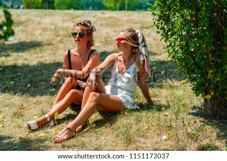 Two beautiful happy women on the grass relaxing in the park in summer.  