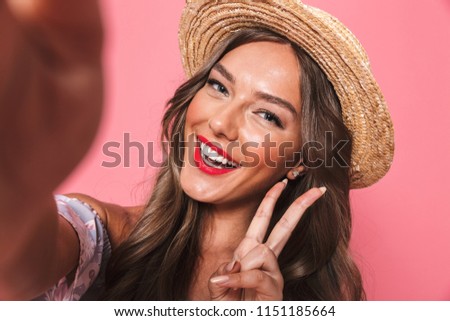 Portrait of a happy young girl in summer clothes taking a selfie with outsretched hand over pink background