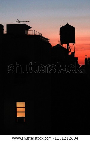 NYC building and water tower at sunset with light on in window