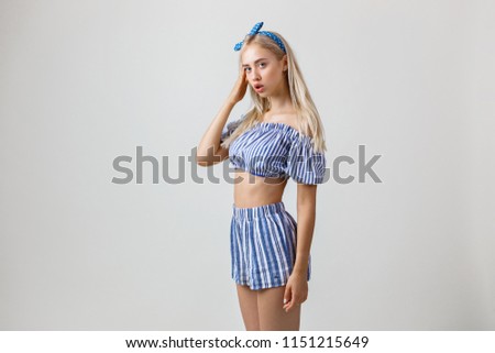 Blonde girl in summer outfit is holding hand on cheek standing over white background with with thoughtful and puzzled expression on face