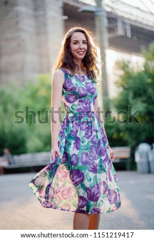Portrait of a young and attractive brunette woman silhouetted against the sun and the Brooklyn bridge in the summer at sunset. She is tall, slim and elegant; she is smiling for the head shot.