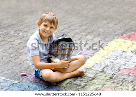 Little active kid boy drawing knight castle and fortress with colorful chalks on asphalt. Happy child with big helmet having fun with playing knight game and painting