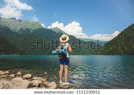 Beautiful girl traveler in a hat stands on a lake in the background of the mountains