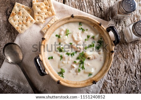 A delicious creamy white fish chowder with haddock, cod, potato, and onion garnished with parsley and served with soda crackers.
