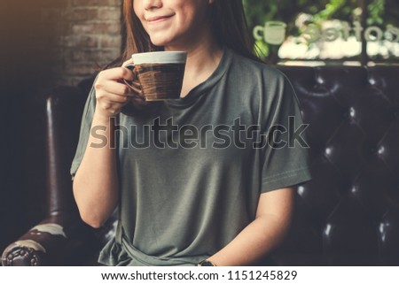 Closeup image of an Asian woman holding and drinking hot coffee with feeling good in vintage cafe