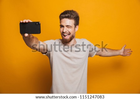 Image of handsome cheerful man standing isolated over yellow wall backgroung make a selfie by smartphone showing copyspace.