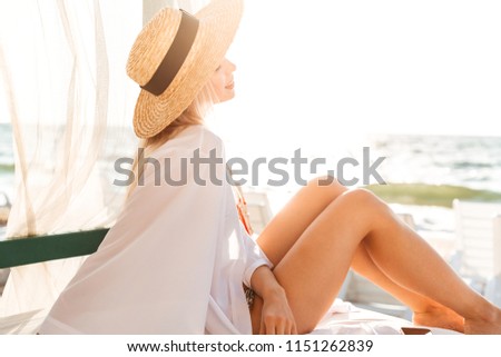 Romantic young girl in summer hat and swimwear resting at the sunny beach