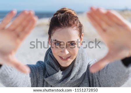 Pretty young woman framing the viewer with her hands to help her visualise an idea with focus to her smiling face