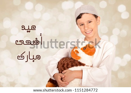 Greeting Card : Eid Adha Mubarak - Arabic Translation : Happy Sacrifice Feast - Happy little boy playing with his sheep toy - celebrating Eid ul Adha Royalty-Free Stock Photo #1151284772