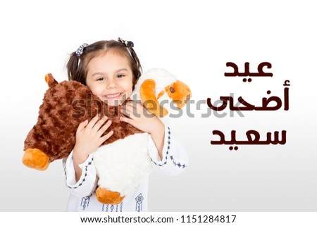 Greeting Card : Eid Adha Saeed - Arabic Translation : Happy Sacrifice Feast - Happy little girl playing with her sheep toy - celebrating Eid ul Adha Royalty-Free Stock Photo #1151284817