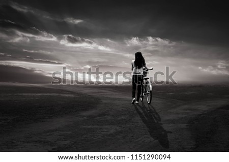 Black and white photo. A girl strolls a bike lost in the sunset.