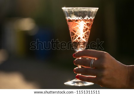 A glass of wine is being held by a young woman with the sun backlighting.
