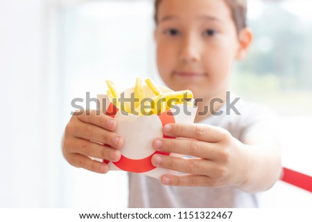 The boy 8 years old holds out the fries in paper box, fast food concept