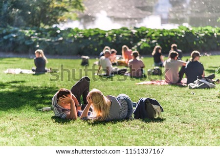 Relaxing summer day in a Danish park, people lounging on the grass, pond water in the background. Concept of hygge. Royalty-Free Stock Photo #1151337167
