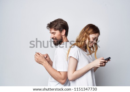 a man and a woman in white T-shirts stand with their backs to each other with telephones in their hands                            