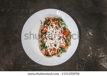 Prepared for baking fillets of poultry with herbs, tomatoes, cheese with cheese on a white plate on a dark concrete background. View from above. The concept of healthy proper nutrition.