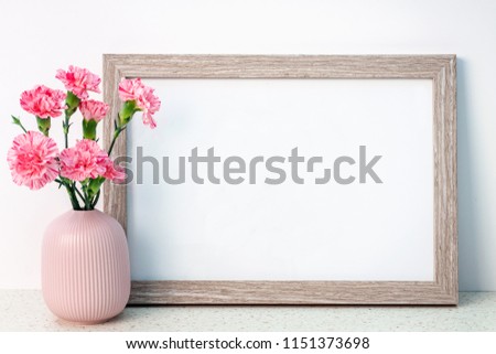 Wooden frame mockup with a pink notched vase with carnations on a desk with the terrazzo pattern
