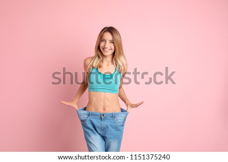 Young slim woman in old big jeans showing her diet results on color background Royalty-Free Stock Photo #1151375240