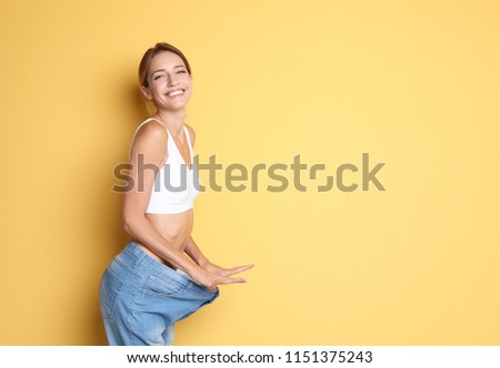 Young slim woman in old big jeans showing her diet results on color background Royalty-Free Stock Photo #1151375243