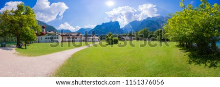 Koenigssee is on the border between Germany and Austria. This is the beautiful island on the lake. The forest and the Alps are far away.It is a super wide picture made of a number of photographs.