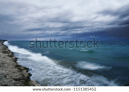 Lubricated small waves with foam during the beginning of the storm in the evening on the shore of the dark sea at the beach of a sea resort photographed for long exposure