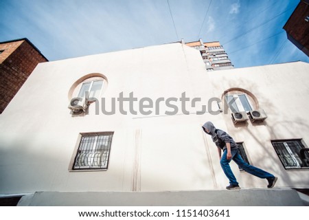 Teenage boy on a street in a big city next to a high-rise building alone. concept of a teenager parkour life. parkour jump on a building background from the side