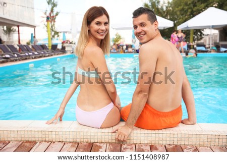 Happy couple resting near blue swimming pool outdoors
