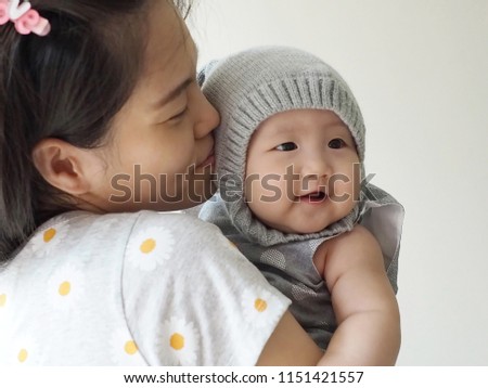 New mother was carrying and kissing her adorable cheeky infant. Asian chubby newborn baby being hold with care by her mom. Concept for Mother’s day, Baby care, Growth and development of infant child.