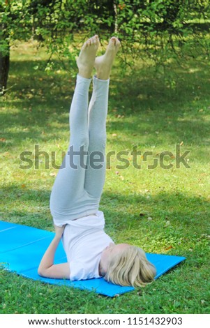 Beautiful blonde preteen girl in light clothing practicing yoga on a mat in the park. Healthy lifestyle. Outdoors workout. 