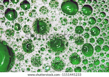 White soap bubbles and suds creating frothy foam on the surface of green water with air pockets of many tiny silver domes on the liquid. Copyspace area for washing up domestic designs, concepts