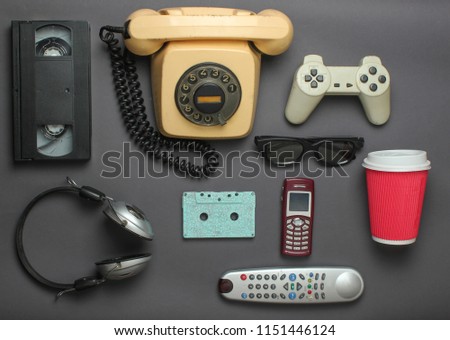 Retro objects on gray background. Rotary telephone, audio cassette, video cassette, gamepad, 3d glasses, tv remote, headphones, push-button phone. Analog media technology of the past. Flat lay.
