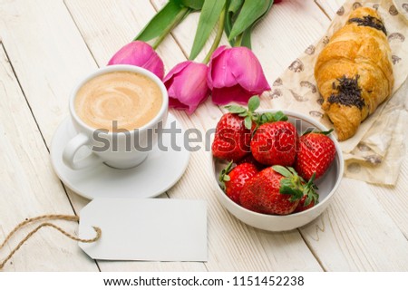 Cup of coffee, tulips, croissant, strawberries on wooden background