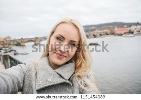 A beautiful young blond woman or tourist doing selfie or photographing herself in Prague in the Czech Republic. Charles Bridge in the background.