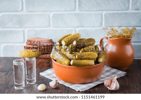 Pickled cucumbers in clay bowl, vodka in wine-glasses, bread and salo on dark wooden table. Traditional Russian snack. Soft focus