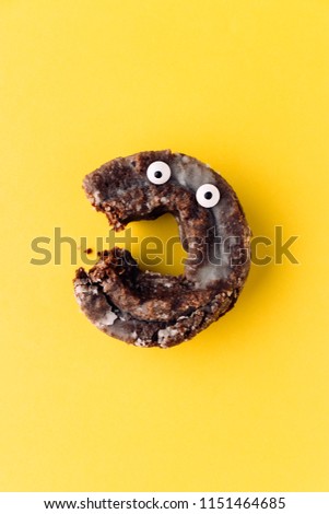 Funny shock face glazed chocolate cake donut on a pastel yellow background, creative minimal Halloween concept