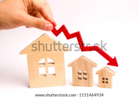 The hand holds a red arrow above the wooden houses down. The houses are decreasing. The concept of falling demand and supply in the real estate market. Economic crisis. The fall in prices.